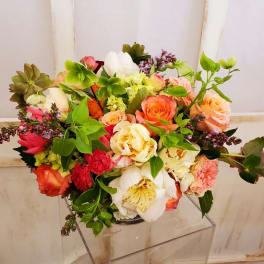 Mixed bouquet of roses, peonies, and other blooms in a clear vase