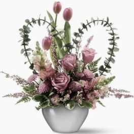 Pink tulips and roses arranged in a gray vase with heart-shaped greenery