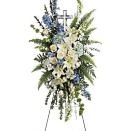 Standing funeral spray with white lilies, blue flowers, and a cross