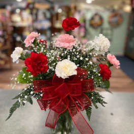 Bouquet of red, pink, and white carnations in a glass vase with a red ribbon