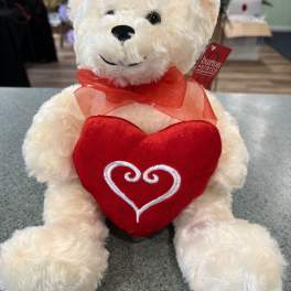 White teddy bear holding a red heart and wearing a red ribbon