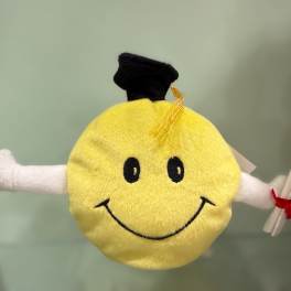 Smiling yellow plush graduation character with a black cap and diploma