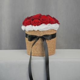 Red roses arranged in a woven hatbox with a black ribbon