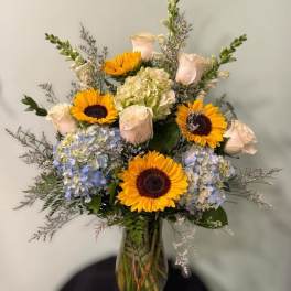 Bouquet of sunflowers, pale roses, and hydrangeas in a glass vase