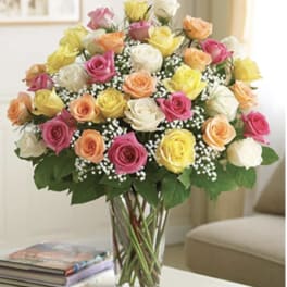 Mixed roses in pink, yellow, peach, and white in a clear glass vase