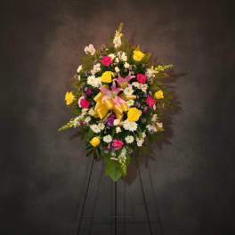 Standing floral spray with pink lilies, yellow roses, and a gold ribbon on an easel