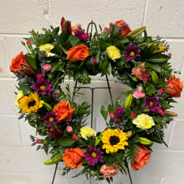 Heart-shaped floral wreath with orange roses and mixed blooms on a metal stand