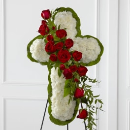 Standing cross of white flowers with red roses and cascading greenery on a metal easel.