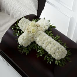 White floral cross with cream roses resting on a dark wood casket.