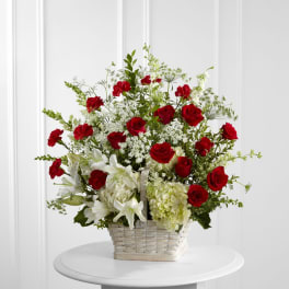 Tall basket arrangement of red roses, white lilies, and hydrangeas in a white woven basket