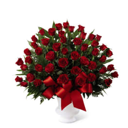 Large arrangement of red roses in a white pedestal vase with a red bow