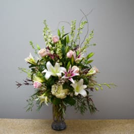 Tall arrangement of white lilies and pale pink roses in a clear glass vase