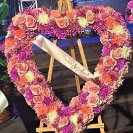 Heart-shaped floral wreath with pink roses and purple flowers on an easel