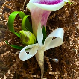 A calla lily boutonniere with white ribbon on brown filler