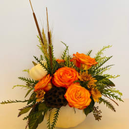 Orange roses arranged in a white pumpkin container with dried wheat accents