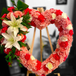 Heart-shaped floral wreath with pink and red carnations and white lilies