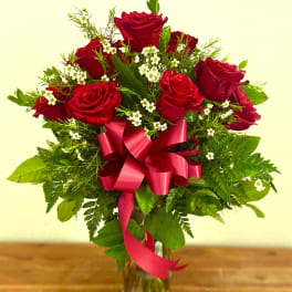 Red roses arranged in a clear glass vase with a pink ribbon