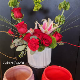 Red roses and pink lilies in a white vase with a heart-shaped greenery arch