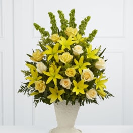 Tall yellow lilies and cream roses in an ivory pedestal vase with vertical green accents
