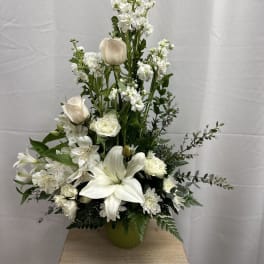 Tall white floral arrangement with lilies and roses in a green vase
