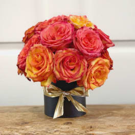 Bouquet of pink and orange roses in a black box tied with a gold ribbon