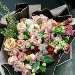Bouquet of blush and peach roses with pink accents wrapped in black paper