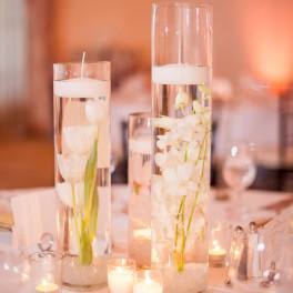 Tall glass vases with white flowers and floating candles on a table