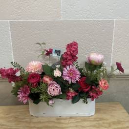 Pink and red mixed flower arrangement in a white container