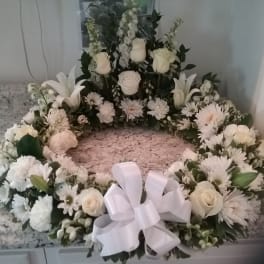 White floral wreath with roses, lilies, and daisies tied with a white bow