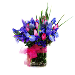 Blue and pink mixed flowers in a glass vase with a pink ribbon