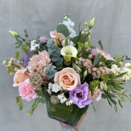 Mixed pastel bouquet with roses, calla lilies, and purple blooms in a glass vase