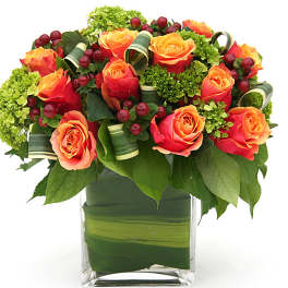 Orange roses arranged in a clear square vase with green accents