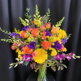 Bright mixed bouquet of roses, gerbera daisies, and orchids in a clear vase