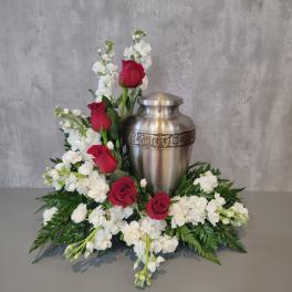 Red roses and white flowers arranged around a silver urn.