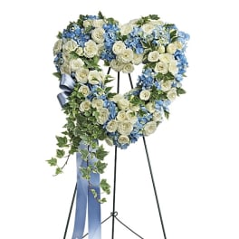 Heart-shaped floral wreath of white roses and blue flowers on a stand