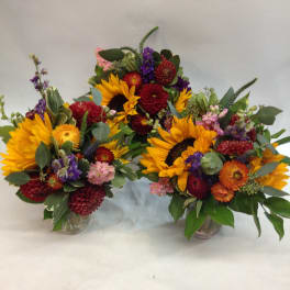 Three colorful flower arrangements in glass vases with sunflowers and mixed blooms
