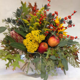 Autumn bouquet with yellow flowers, red berries, and apples in a glass vase