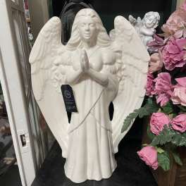 Ceramic praying angel statue beside pink artificial flowers
