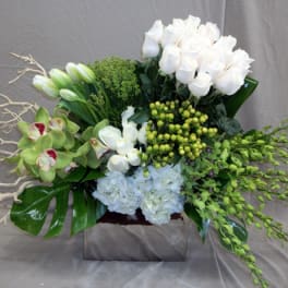 White floral arrangement with orchids and roses in a square vase