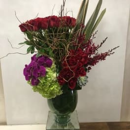 Tall bouquet of red roses, purple orchids, and green hydrangeas in a glass vase