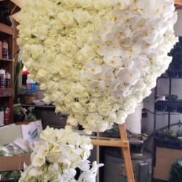 Heart-shaped floral arrangement of white roses and orchids on an easel