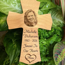 Wooden memorial cross with engraved portrait and text among green foliage