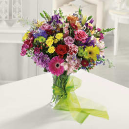 Bright mixed bouquet of multicolored flowers in a clear glass vase with a green ribbon bow