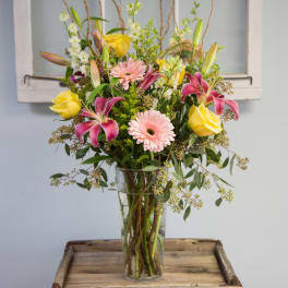 Mixed bouquet of pink lilies, yellow roses, and pale gerbera daisies in a glass vase