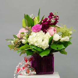 Mixed pink and white bouquet in a purple vase with a candy bag beside it