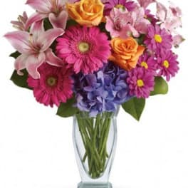 Mixed bouquet of pink lilies, roses, daisies, and hydrangea in a clear glass vase