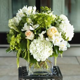White and green floral arrangement in a clear square vase