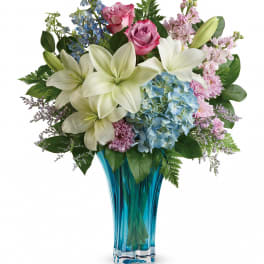 Bouquet of white lilies, pink roses, and blue hydrangeas in a blue glass vase