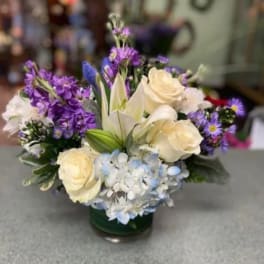 Bouquet of cream roses, lilies, and purple flowers in a glass vase