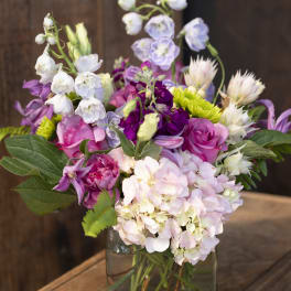 Mixed pink, purple, and white flowers in a square glass vase